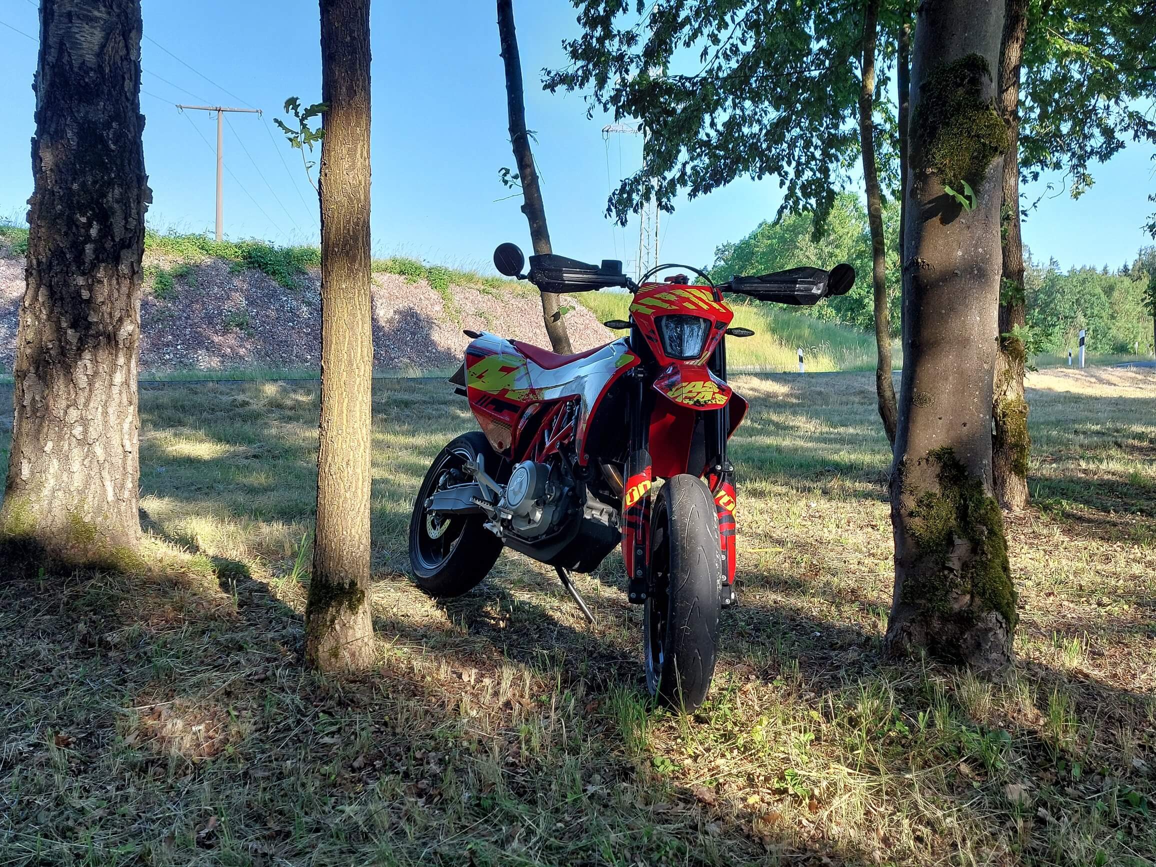 Supermoto im Wald: Eindrucksvolle Aufnahme mit Blick von vorne auf das Motorrad, umgeben von Bäumen und im Hintergrund eine Hauptstraße.